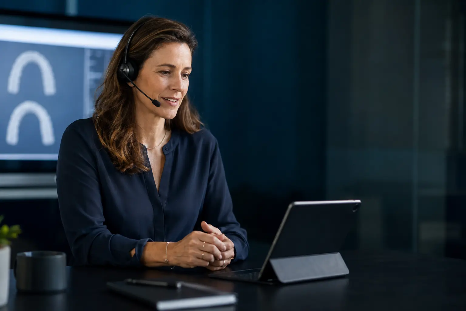An ALLYNAK planner with a headset on a call, digital arches on the screen behind her